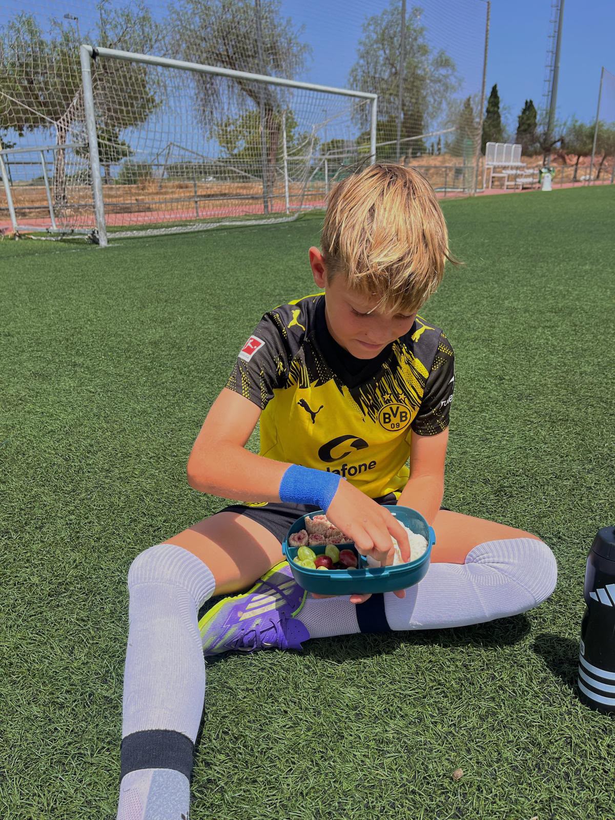 Young soccer player sitting on the field, eating from his game-day snack box